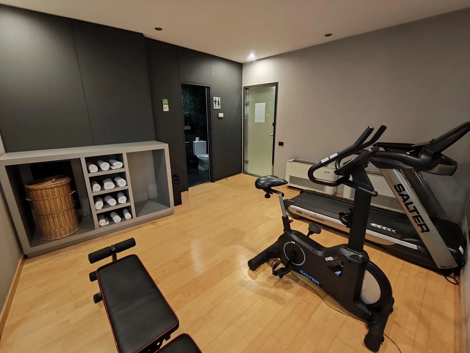 Sala de fitness con cinta de correr, bicicleta y mancuernas frente al espejo